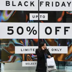 Kobieta z torbami na tle szyldu "Black Friday 50% OFF". Czy to zapowiedź wzrostu cen w koszyku zakupowym przed promocjami?