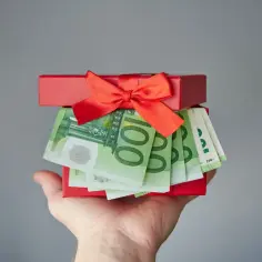 Czerwone pudełko z prezentem wypełnione banknotami euro, trzymane na dłoni.