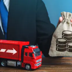Biznesmen z workiem pieniędzy i czerwona ciężarówka symbolizują, jak optymalizować koszty transportu w handlu towarami masowymi.