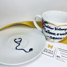 Biała filiżanka i spodek z motywem stetoskopu i napisem "Doktor Katarzyna".