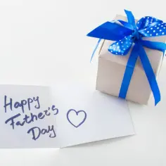 Prezent na Dzień Ojca: kartka z życzeniami "Happy Father's Day" i sercem, obok pudełko ozdobione niebieską wstążką w kropki.