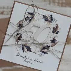 Elegancka kartka z życzeniami na 50 urodziny, ozdobiona wiankiem z suszonych traw i kwiatów. Idealna inspiracja, co kupić kobiecie na 50 urodziny.