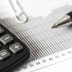 Kalkulator i długopis na papierze z wykresami. Planujesz handel i zastanawiasz się, jakie są progi podatkowe w handlu dla ryczałtowców 2026?