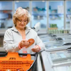 Starsza pani w sklepie analizuje cenę ryby, zastanawiając się nad skutkami wprowadzenia podatku od sprzedaży detalicznej dla konsumenta.