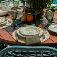 Oto inspiracja, jak udekorować stół na przyjęcie w ogrodzie w stylu boho: talerze z motywem cytrusów, zielone kieliszki i plecione podkładki tworzą letni klimat.