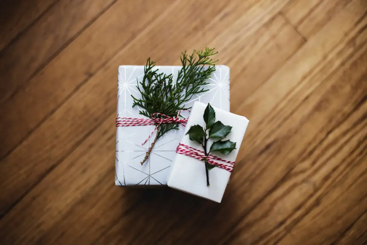 Dwa elegancko zapakowane prezenty z gałązkami iglaków i ostrokrzewu. Rosnąca świadomość ekologiczna to przyczyny mody na prezenty ekologiczne zero waste i less waste.