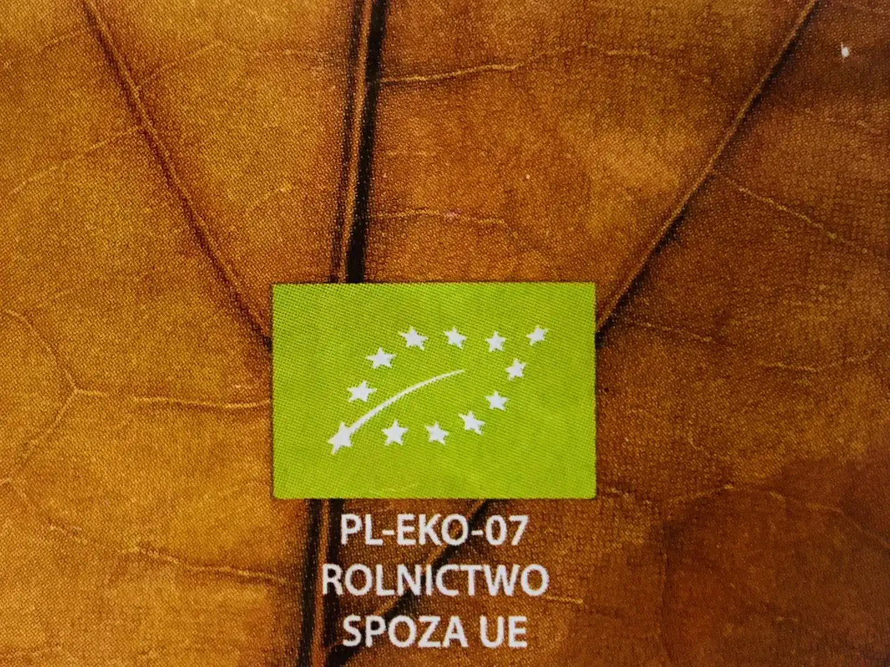 Zielony certyfikat PL-EKO-07 na tle liścia. Produkty bio i eko mają wyższe ceny przez koszty certyfikacji i mniejszą skalę produkcji.