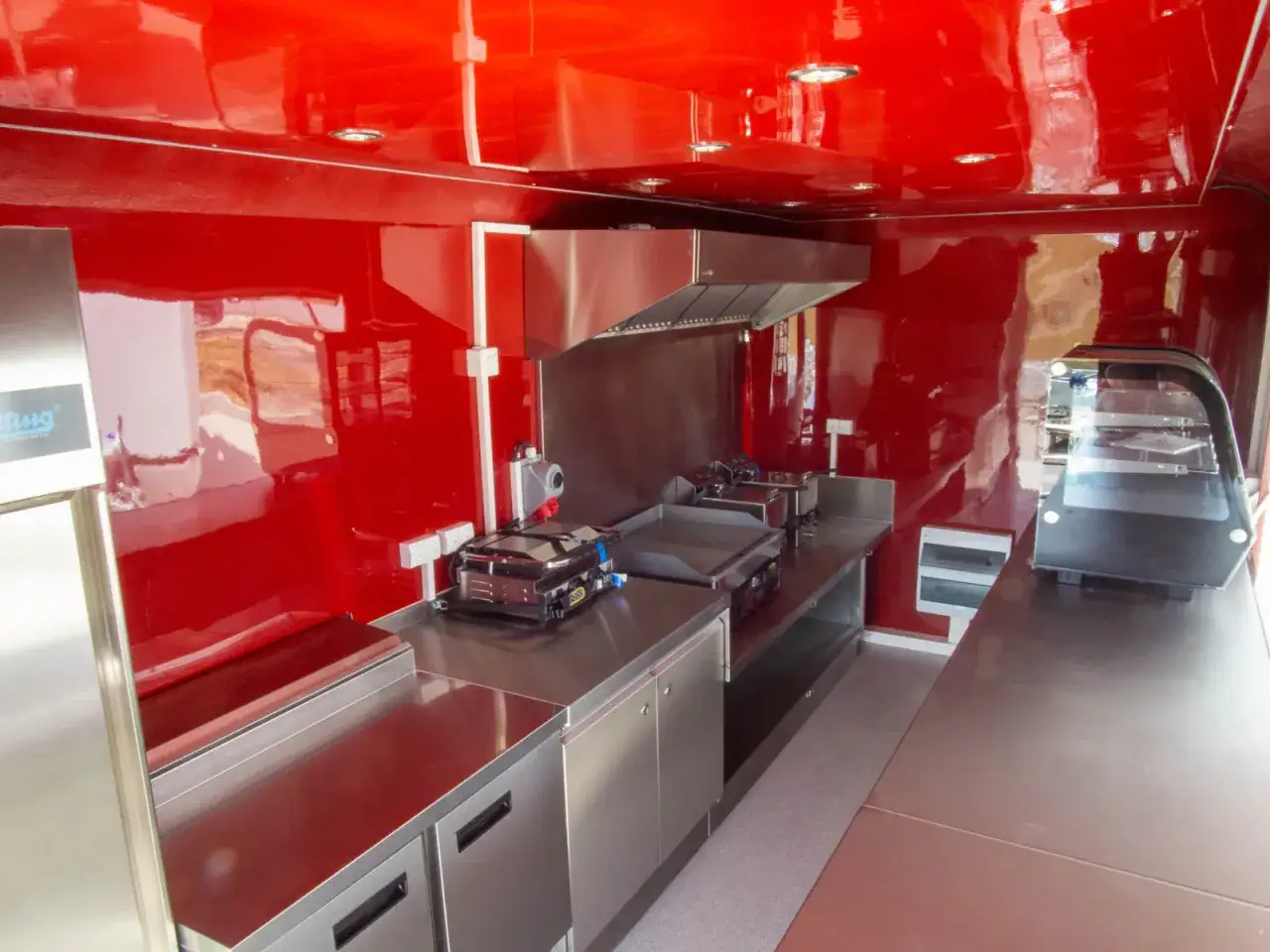 Wnętrze food trucka z czerwonymi ścianami i sufitem, stalowymi blatami, grillem i witryną. Spełnia wymogi sanepidu dla handlu obwoźnego.
