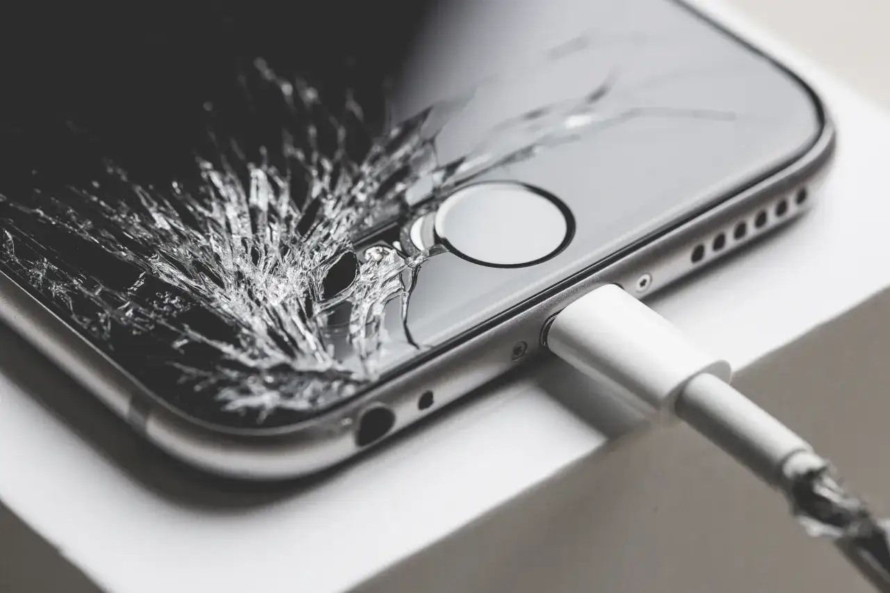 Pęknięty ekran smartfona z podłączonym kablem. Sprawdź objawy uszkodzonego wyświetlacza w używanym smartfonie przed zakupem.