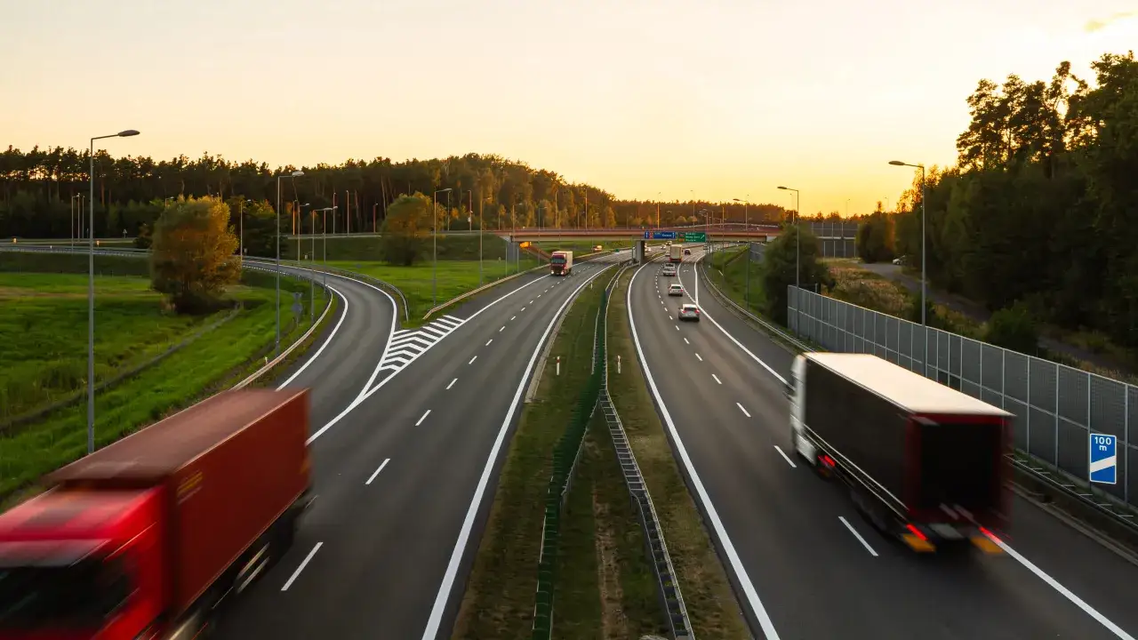 Ciężarówki na autostradzie o zachodzie słońca. Klucz do tego, jak optymalizować koszty transportu w handlu towarami masowymi, leży w efektywnym zarządzaniu logistyką.