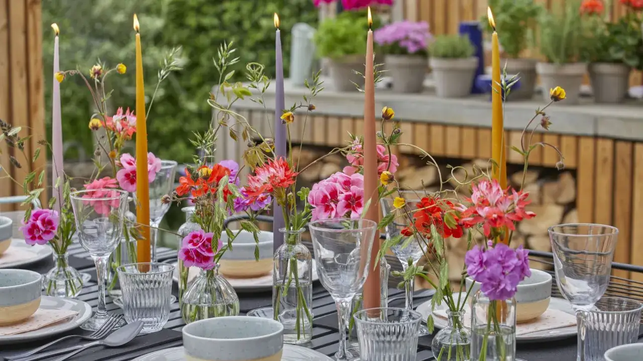 Jak udekorować stół na przyjęcie w ogrodzie w stylu boho: kolorowe świece, dzikie kwiaty w małych wazonach i szkło tworzą magiczną atmosferę.