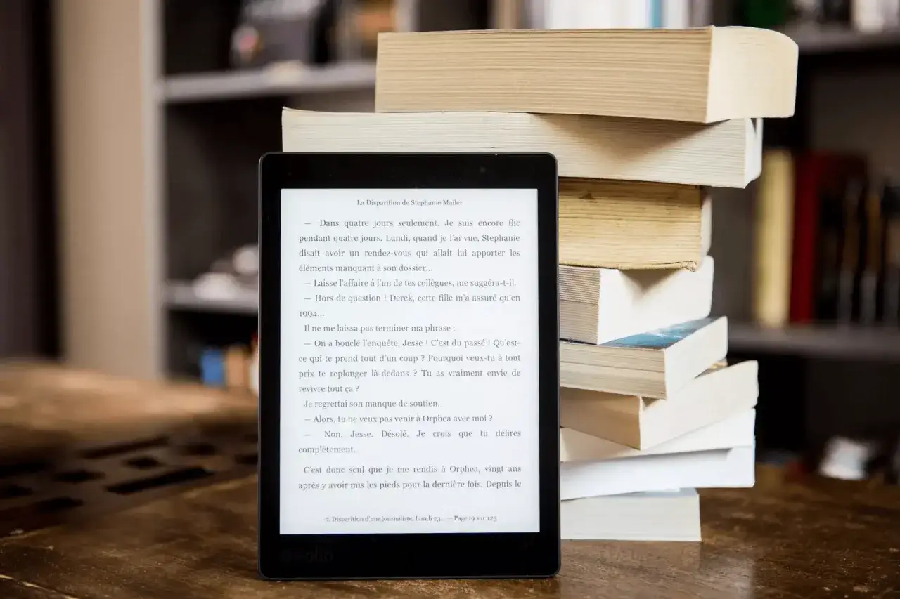 Ranking najlepsze czytniki e-booków z podświetleniem ekranu. E-czytnik Kobo obok stosu książek, idealny do czytania w każdych warunkach.