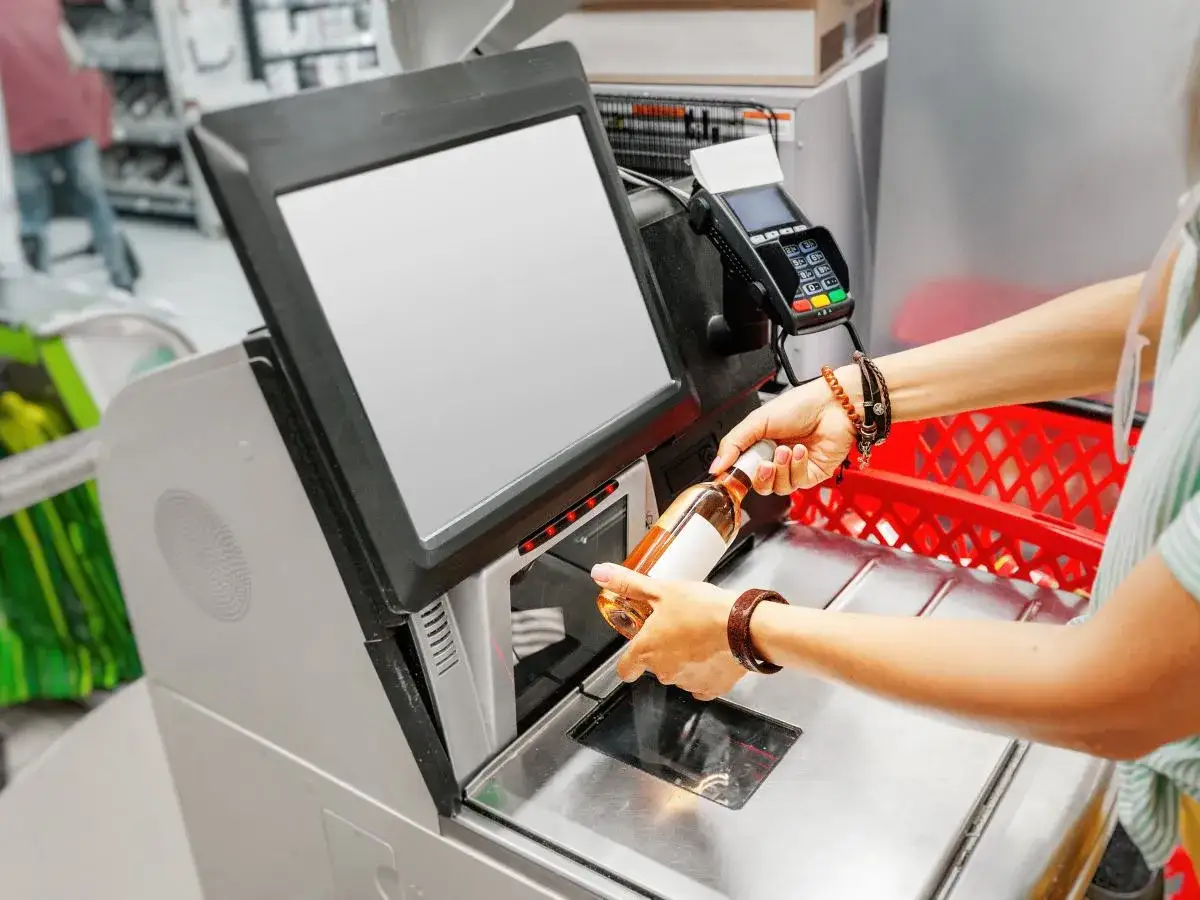Kasy samoobsługowe a zatrudnienie: automatyzacja handlu w praktyce. Klientka skanuje butelkę wina.