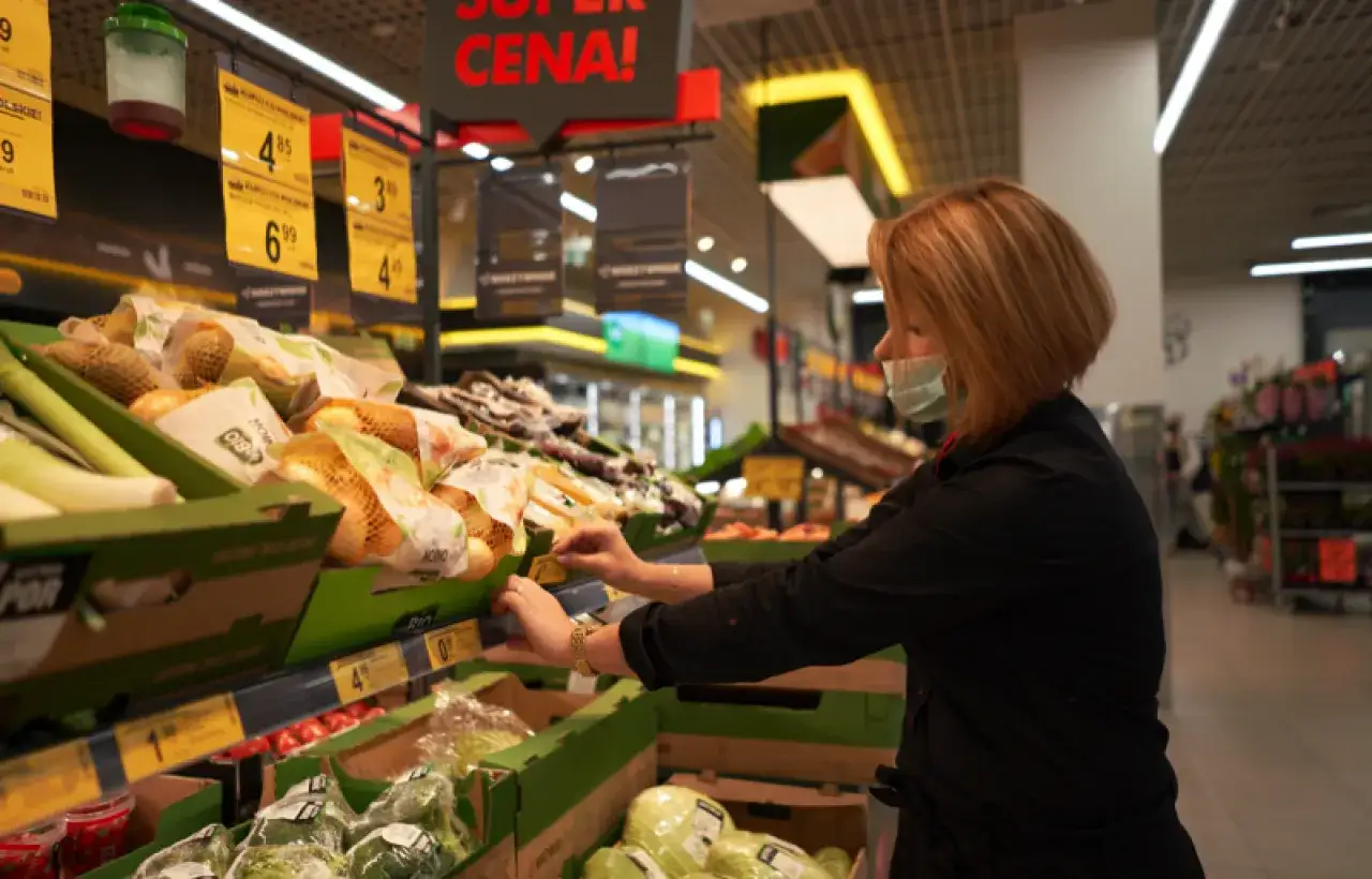Kobieta w masce przegląda warzywa w supermarkecie. Ceny na metkach mogą sugerować objawy nieuczciwych praktyk rynkowych w handlu wielkopowierzchniowym.