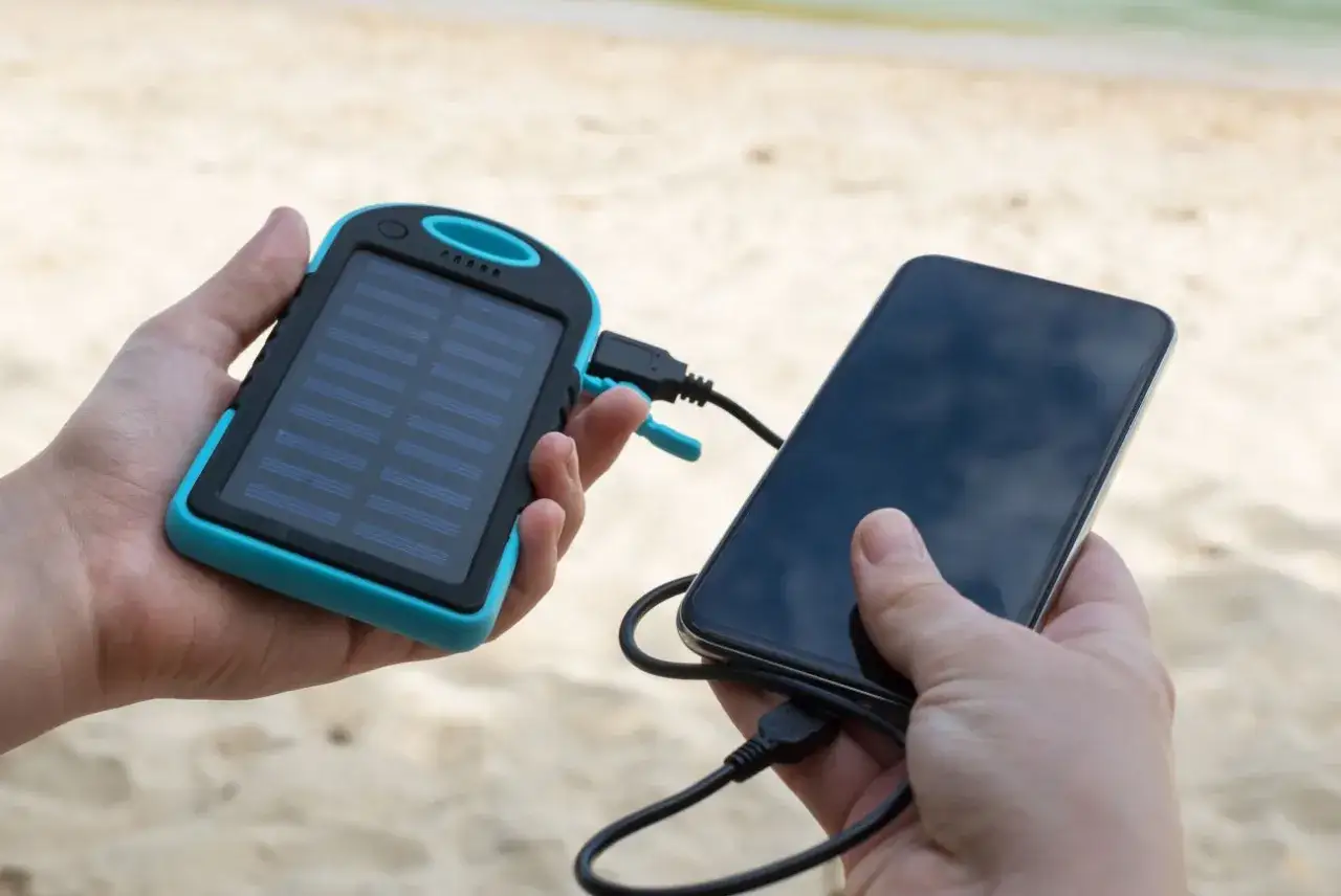 Ręce trzymają powerbank solarny i smartfon. Szybkie ładowanie z rankingiem pojemności to klucz do mobilności na plaży.