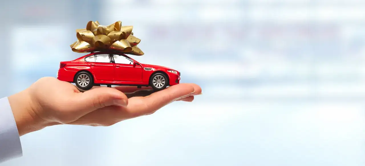 Czerwony model samochodu z kokardą na dachu, trzymany na dłoni. Idealny pomysł na prezent dla fana motoryzacji: przejażdżka lub akcesoria.