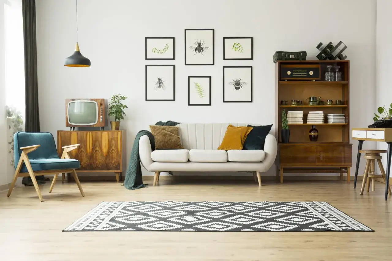 Styl retro w salonie 2026: biała kanapa, turkusowy fotel, drewniane meble, stara telewizja i grafiki z owadami.