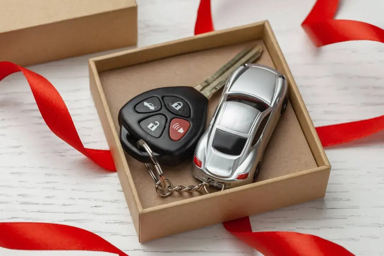 Jak wybrać prezent dla fana motoryzacji? Kluczyki i miniaturowy samochód w pudełku, ozdobione czerwoną wstążką, sugerują przejażdżkę lub akcesoria.