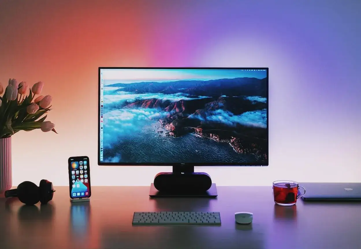 Ranking monitorów do gier 144Hz: płynność obrazu vs cena. Biurko z monitorem, telefonem, słuchawkami i kubkiem herbaty.