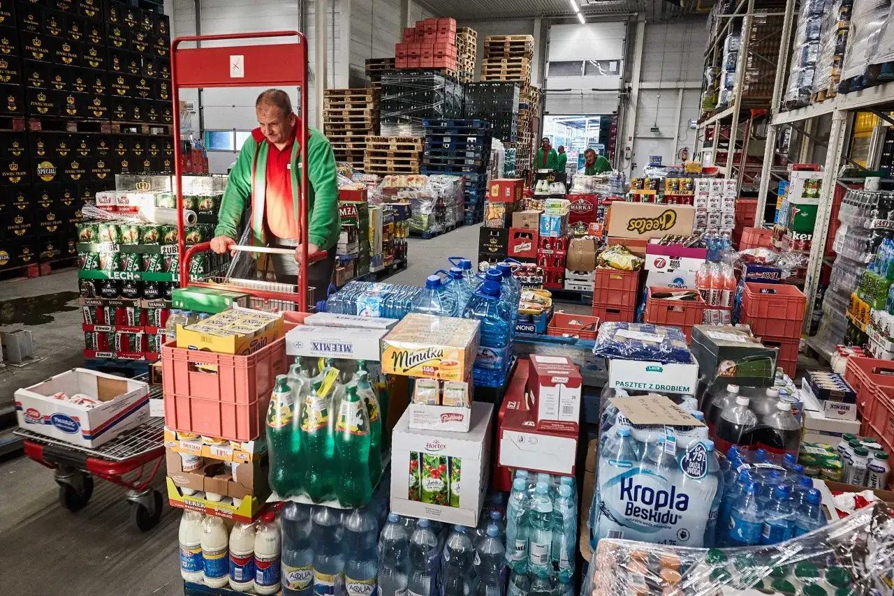 Magazyn z napojami i produktami spożywczymi. Pracownik przesuwa wózek. Różnica między handlem hurtowym a detalicznym w świetle prawa jest tu widoczna w ilościach towaru.