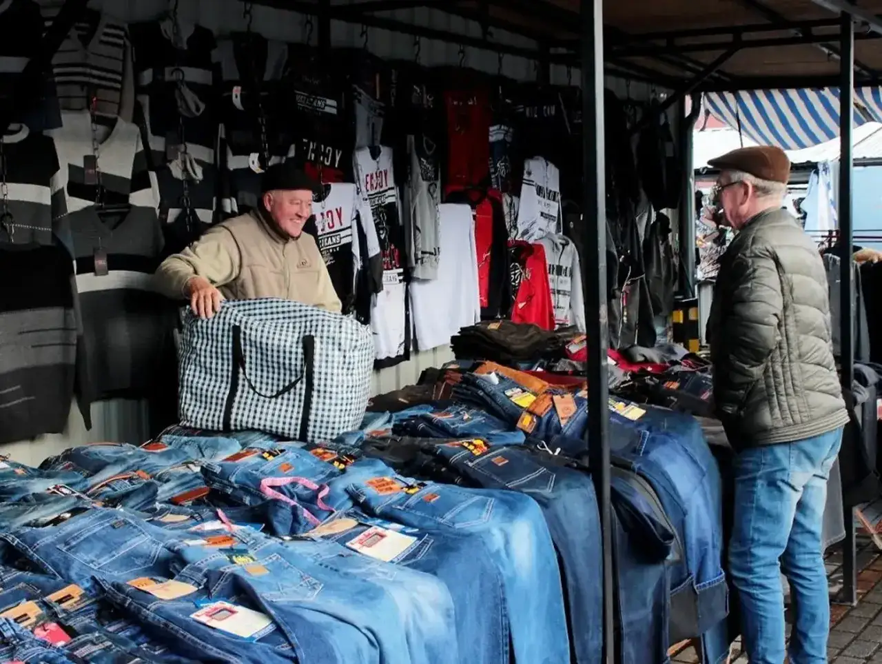 Sprzedawca na targowisku miejskim prezentuje spodnie dżinsowe. Dowiedz się, jakie są zasady handlu na targowiskach miejskich, opłaty i wymogi.